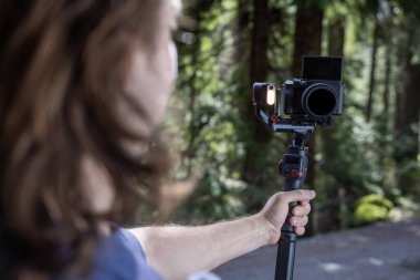 İçerik yaratıcısı, arka planda bulanık bir orman ile doğayı filme almak için bir kamera telsizi kullanıyor.