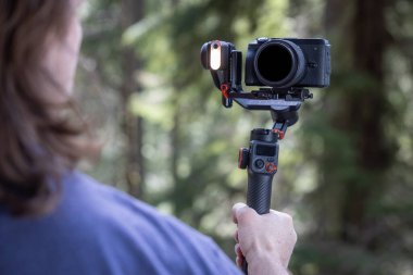 İçerik yaratıcısı, arka planda bulanık bir orman ile doğayı filme almak için bir kamera telsizi kullanıyor.