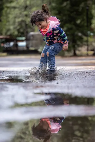 A little girl is playing in the rain and splashing in a puddle. Concept of joy and playfulness, as the child is having fun in the rain