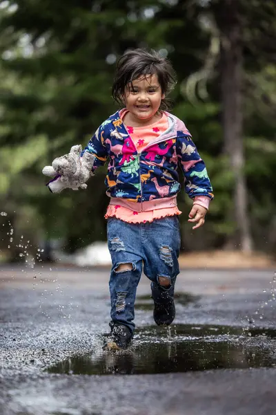 A young girl is playing in the rain, holding a stuffed animal. The scene is playful and joyful, with the girl enjoying the moment and the rain