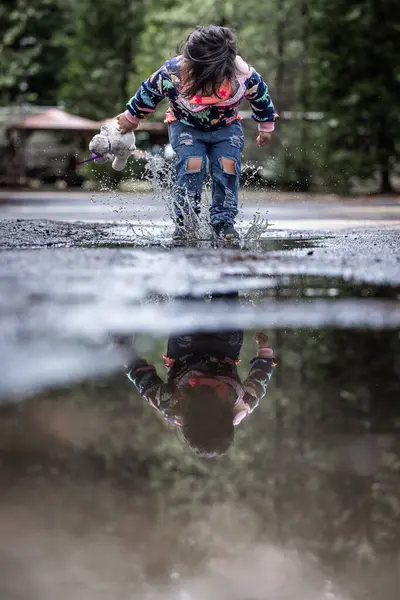 Молода Дівчина Грає Під Дощем Розбризкуючи Воду Тримаючи Фаршировану Тварину Стокове Зображення