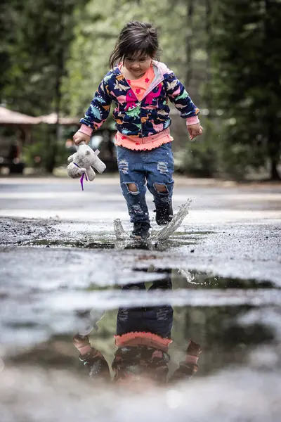 Молода Дівчина Грає Під Дощем Розбризкуючи Воду Тримаючи Фаршировану Тварину Стокове Фото