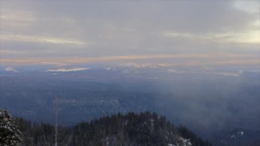 Krater Gölü, Oregon sıradağları bulutlu bir gökyüzü ile uzaktan görülebilir. Gökyüzü mavi ve gri karışımı, resme huzurlu ve huzurlu bir hava veriyor.