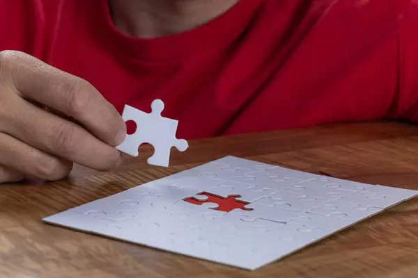 Blank puzzle with the missing piece being held next to the whole with a red placer where the last piece belongs. Concept for problem solving.