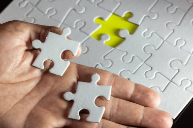 İki beyaz yapboz parçası ve sarı bir parça eksik bir el. Bir bulmacayı çözme kavramı ve onu tamamlamak için eksik parçayı bulmanın önemi.