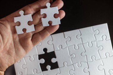 Bir tanesi eksik iki beyaz yapboz parçasını tutan bir el. Tamamlanma ve tatmin kavramı, kayıp parça bulmacayı bitirmenin anahtarıdır.