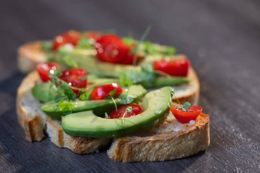 Üstünde avokado ve domates olan bir dilim kızarmış ekşi ekmek.