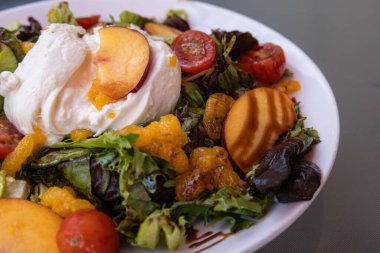 Taze burrata peyniri ve mevsimlik şeftalili yaz salatası. Salatada domates, portakal ve marul gibi birçok farklı malzeme var.