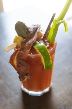 Üstünde pastırma ve turşu olan bir bardak Bloody Mary. İçki limon, zeytin, kereviz ve turşu mızrakla süslenmiş.