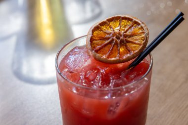Üstünde bir dilim portakal olan pembe bir bardak içki. İçki kısa bir bardakta, siyah bir pipetle servis edilir.
