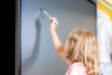 Dijital beyaz tahtaya işaretli bir kız çiziyor. Gülümsüyor ve eğleniyor gibi görünüyor.