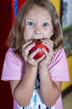 Genç bir kız bir elma yiyor. O, pembe bir gömlek giyiyor. Elma kırmızı ve parlak.