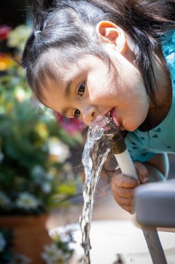 Genç bir kız hortumdan su içiyor. Hortumdan su çıkıyor ve kız da hortumu ağzıyla yakalamaya çalışıyor. Sahne neşeli ve neşeli.