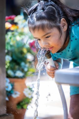 Genç bir kız hortumdan su içiyor. Hortumdan su çıkıyor ve kız da hortumu ağzıyla yakalamaya çalışıyor. Sahne neşeli ve neşeli.