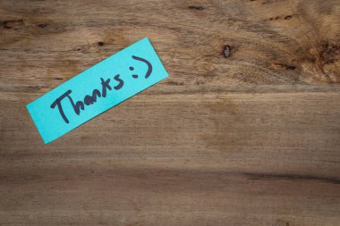 Üzerinde gülen surat olan bir teşekkür notu. Not ahşap bir masanın üzerinde..