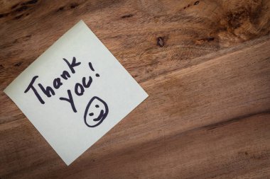Bir kağıt parçasına bir teşekkür notu yazılır ve ahşap bir yüzeye yerleştirilir. Nota gülen bir surat eşlik ediyor. Bu da mesaja olumlu ve dostça bir hava katıyor.