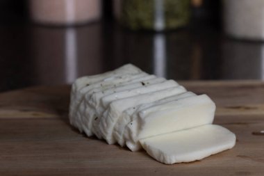 Bir kalıp halloumi peyniri tahta bir kesme tahtasının üzerinde parçalara ayrılır. Peynir beyaz ve Kıbrıs 'tan Halloumi..