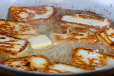 Bir tava halloumi peyniri altın kahverengi bir kabukla gösterilir. Sıcak tereyağında pişirmek. Yemek lezzetli ve davetkar görünüyor.
