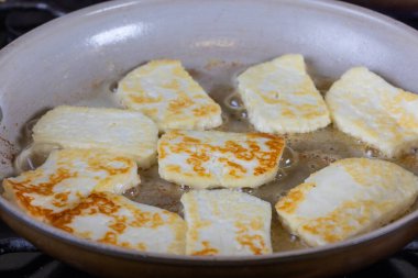Bir tava halloumi peyniri altın kahverengi bir kabukla gösterilir. Sıcak tereyağında pişirmek. Yemek lezzetli ve davetkar görünüyor.