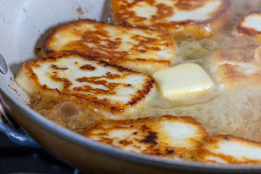 Bir tava halloumi peyniri altın kahverengi bir kabukla gösterilir. Sıcak tereyağında pişirmek. Yemek lezzetli ve davetkar görünüyor.