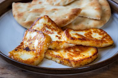 Bir tabak kızarmış halloumi peyniri ve yanında da pita ekmeği. Yemekler altın sarısı ve lezzetli görünüyor..