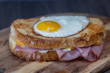 Croque Madame veya ızgara peynirli jambon ve yumurtalı ahşap kesim tahtası. Sandviç kızartılmış ve cıvık sarısı var.