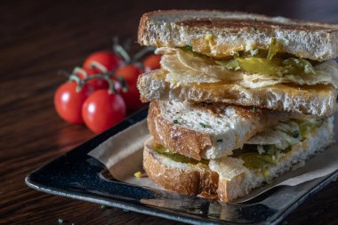 Bir tabakta patates cipsi ve yanında domates olan bir sandviç. Sandviç ikiye bölünmüş ve üstüne istiflenmiş..