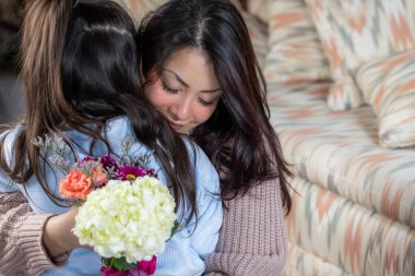 Genç bir anne, Anneler Günü hediyesi olarak küçük kızından bir buket çiçek tutuyor. Kadın gülümsüyor ve kız ona bakıyor. Çiçekler pembe ve beyaz.