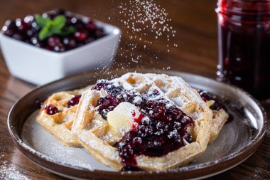 Üzerine tereyağı, taze yaban mersini ve üzerine pudra şekeri serpilmiş böğürtlen reçeli serpiştirilmiş altın waffle 'ların yakın çekimi. Kırsal kahvaltı ya da tatlı yemek fotoğrafçılığı gurme, ev yapımı..