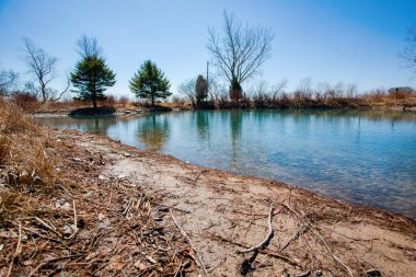 Ontario Canada, Sarnia 'da bir gölet öğleden sonra manzarası. Suyun yüzeyine yansıyan bulutlarla sazlıklar, ağaçlar ve mavi gökyüzü.