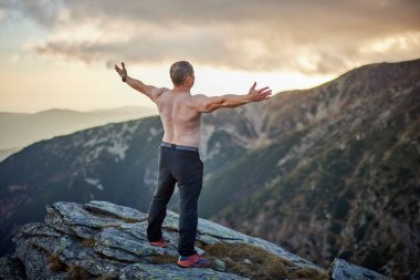 Çıplak göğüslü orta yaşlı adam kayalık dağların tepesinde