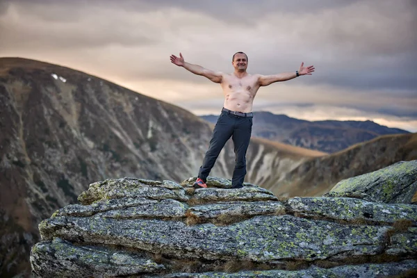 Çıplak göğüslü orta yaşlı adam kayalık dağların tepesinde