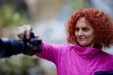 Dijital kamerayla fotoğraf çeken kıvırcık saçlı bir kadının portresi.