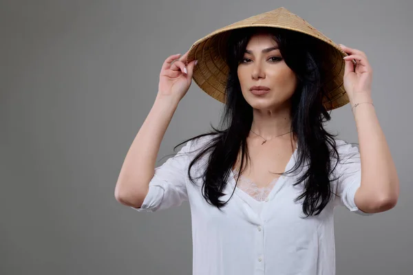 Portrait of a beautiful brunette woman with a Vietnamese hat posing in the studio.