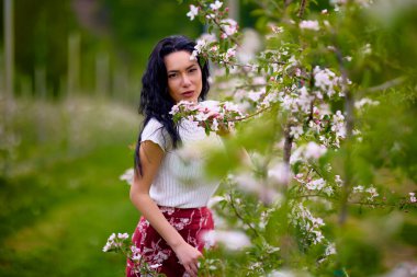 Çiçekli bir elma bahçesinde güzel esmer bir kadının portresi.