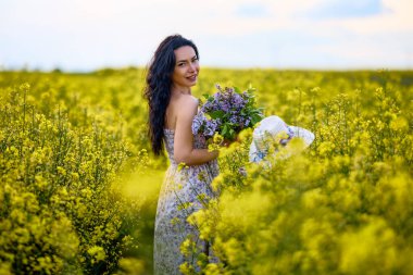 Baharda kolza tohumu tarlasında esmer bir kadının portresi.