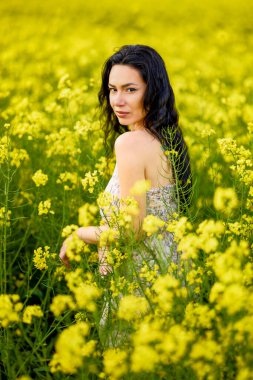 Baharda kolza tohumu tarlasında esmer bir kadının portresi.