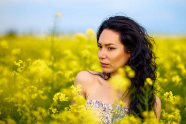 Baharda kolza tohumu tarlasında esmer bir kadının portresi.