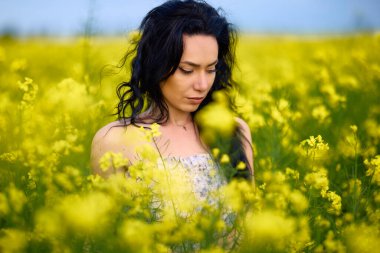 Baharda kolza tohumu tarlasında esmer bir kadının portresi.