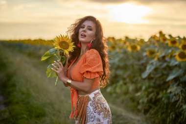 Güneşli bir günde gün batımında ayçiçeği tarlasının yanında güzel bir kadının portresi..