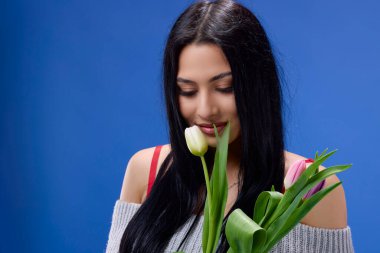 Elinde lalelerle stüdyoda mavi arka planda poz veren güzel bir genç kadın.