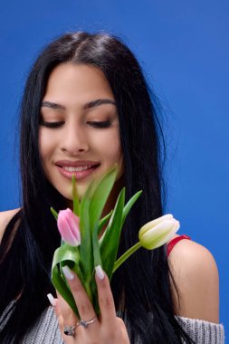Elinde lalelerle stüdyoda mavi arka planda poz veren güzel bir genç kadın.