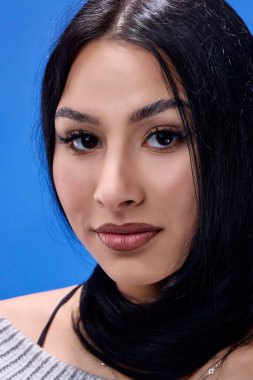 Stüdyoda mavi arka planda poz veren güzel esmerin portresi.