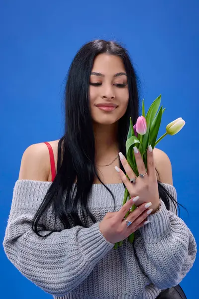 stock image A beautiful young woman with tulips in her hand posing in the studio on a blue background