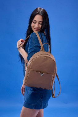 Sırt çantasıyla stüdyoda poz veren uzun saçlı genç bir esmer, okula geri dönüyor..