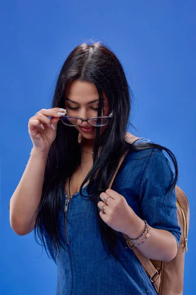 Sırt çantasıyla stüdyoda poz veren uzun saçlı genç bir esmer, okula geri dönüyor..