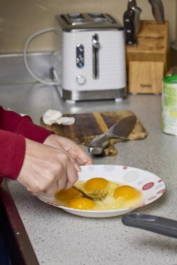 Bir kadının elleri çatalla yumurtayı tabakta karıştırıp hazırlıyor..