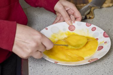 Bir kadının elleri çatalla yumurtayı tabakta karıştırıp hazırlıyor..