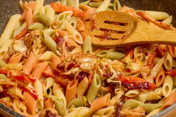 pasta with vegetables in a pan while they are cooked on the stove.