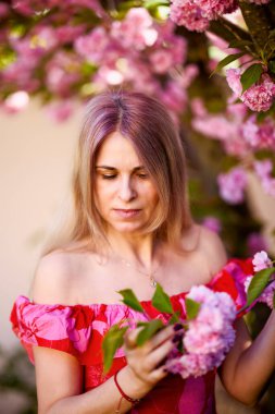 Bir bahar günü çiçek açan Japon kiraz ağacının yanında sarışın bir kadının portresi..